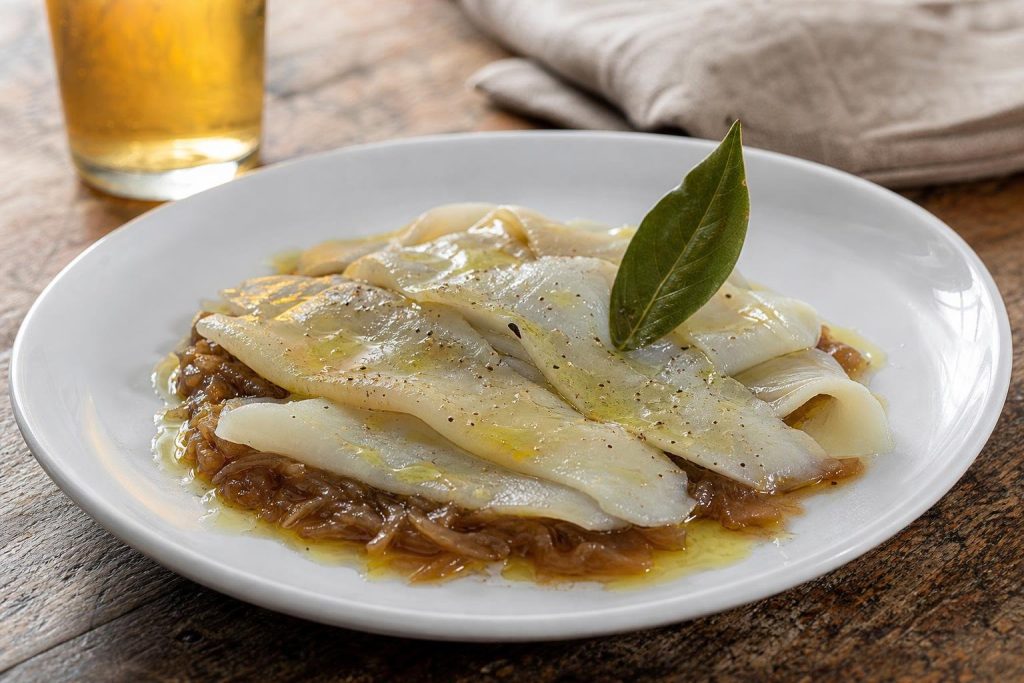 Carpaccio di baccalà affettato sottile su un letto di cipolle caramellate alla birra