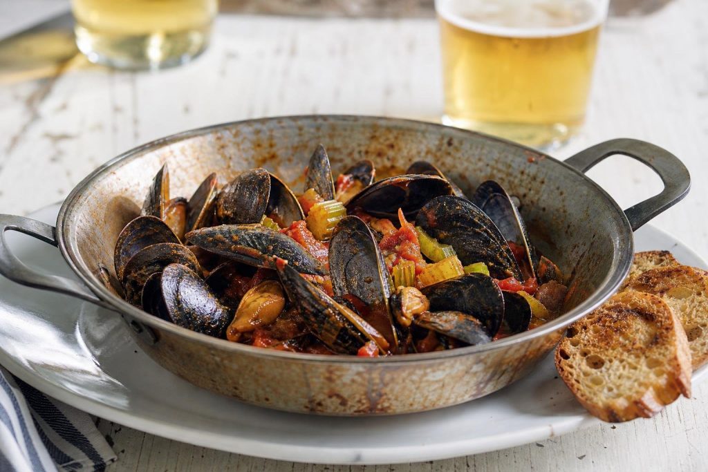 Cozze con pomodoro e sedano in un tegame, con crostoni di pane tostato