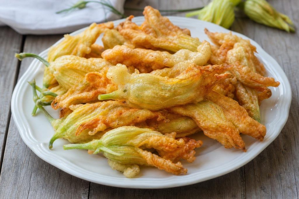 Fiori di zucca in pastella alla birra dorati e croccanti su un piatto bianco